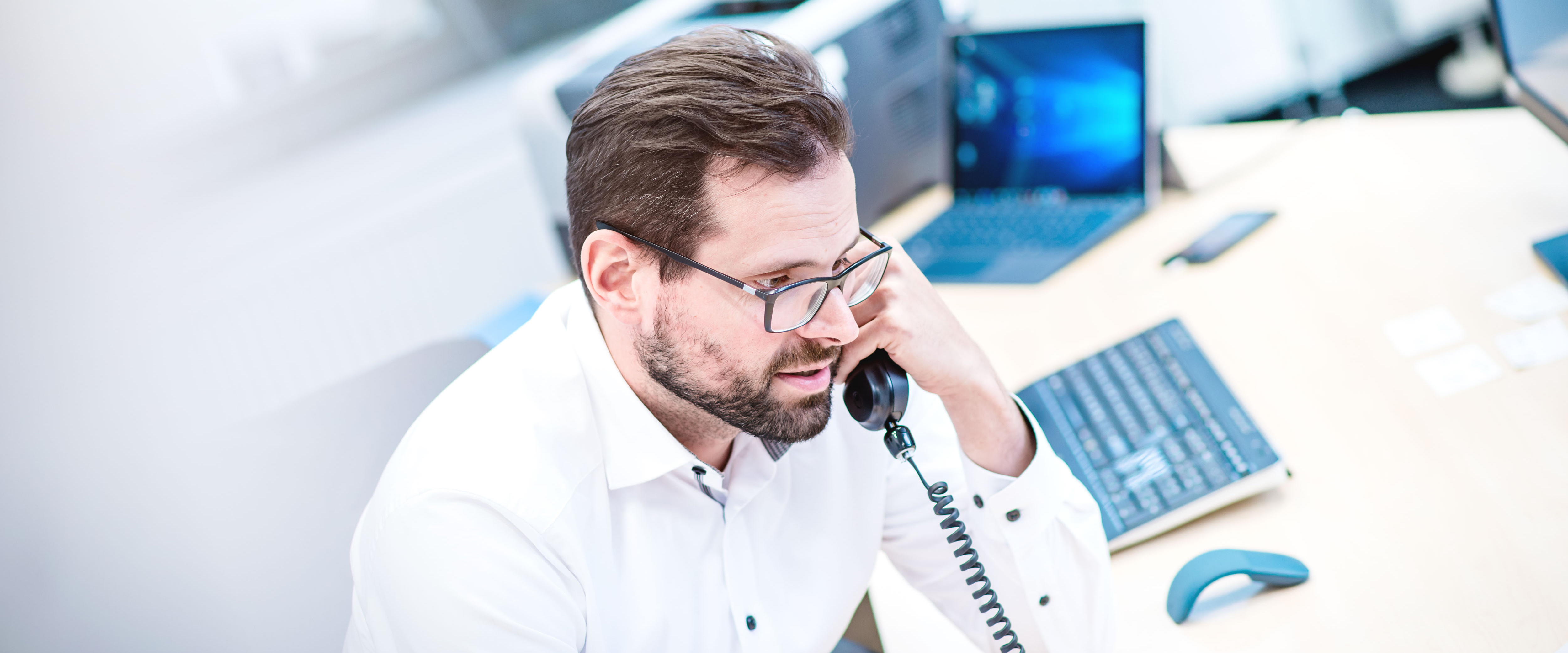 ein Mann sitzt telefonierend an seinem Arbeitsplatz